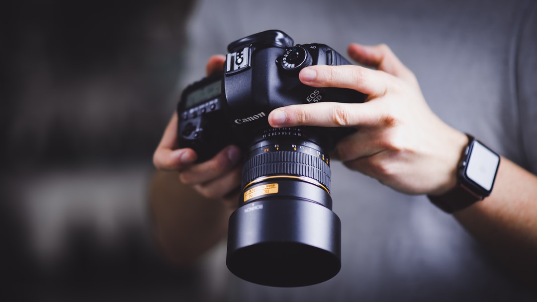 Person holding a canon camera and wearing a watch